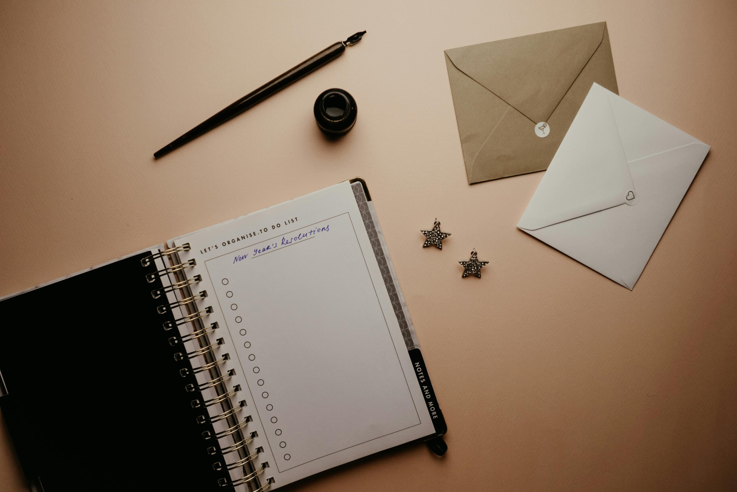 Top view of a planner with envelopes, fountain pen, and ink on a neutral background.